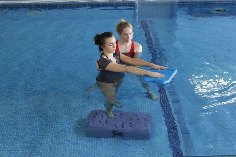 Physical therapist assisting patient with aquatic therapy exercises in therapeutic pool for neurological rehabilitation